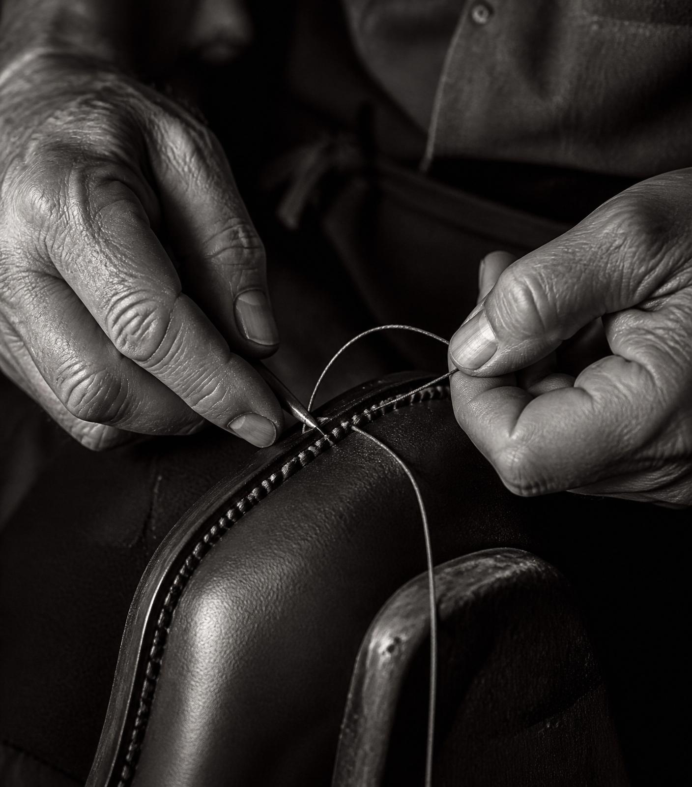 Main d'artisan cousant le trépointe d'une chaussure.