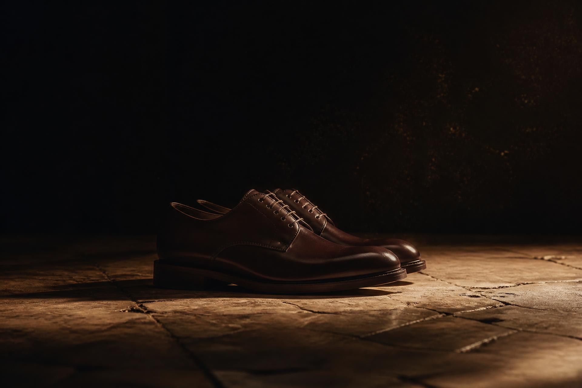 Une paire de derbies en cuir cognac posée sur un dallage de pierre ancienne.